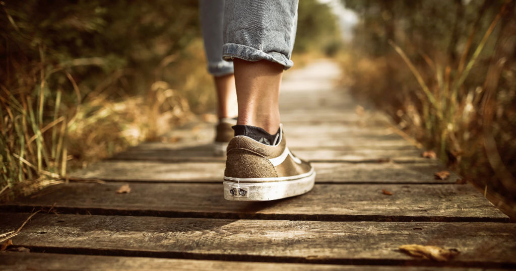 A student with jeans and tennis shoes steps out onto a long, wood bridge making a path into the distance