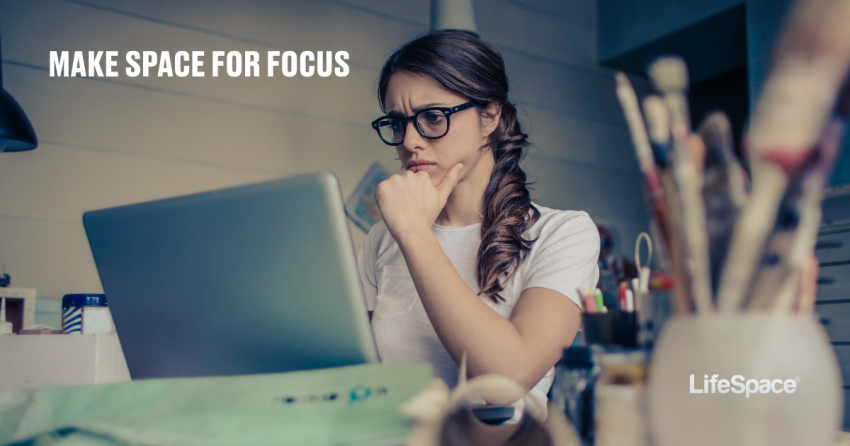 Young professional woman focuses intently on her laptop with paint brushes in the foreground