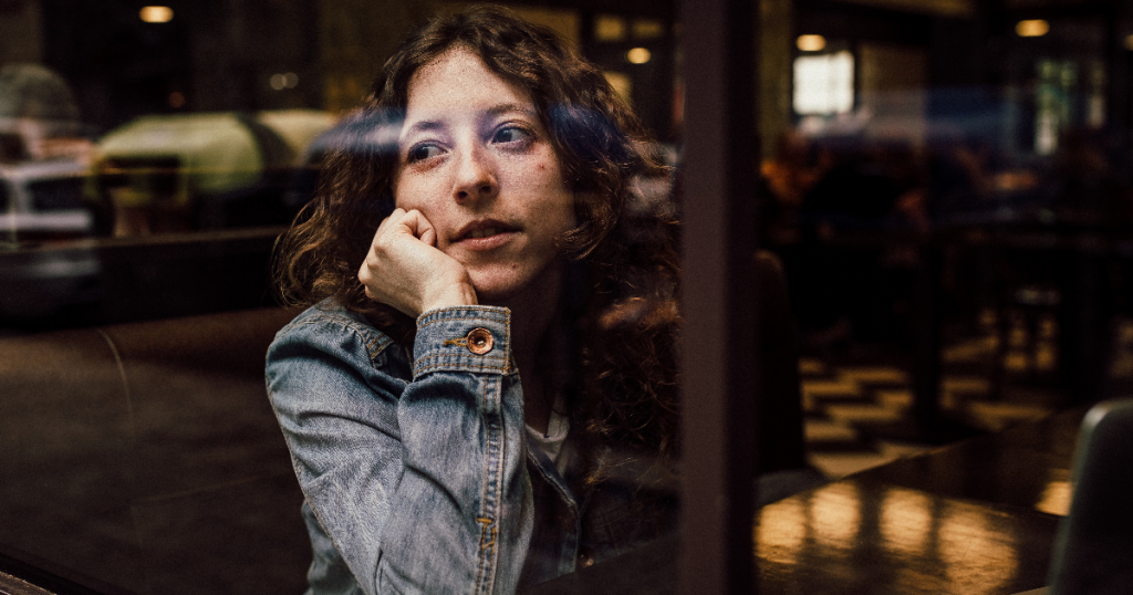 young woman stares listlessly out of a coffeeshop window
